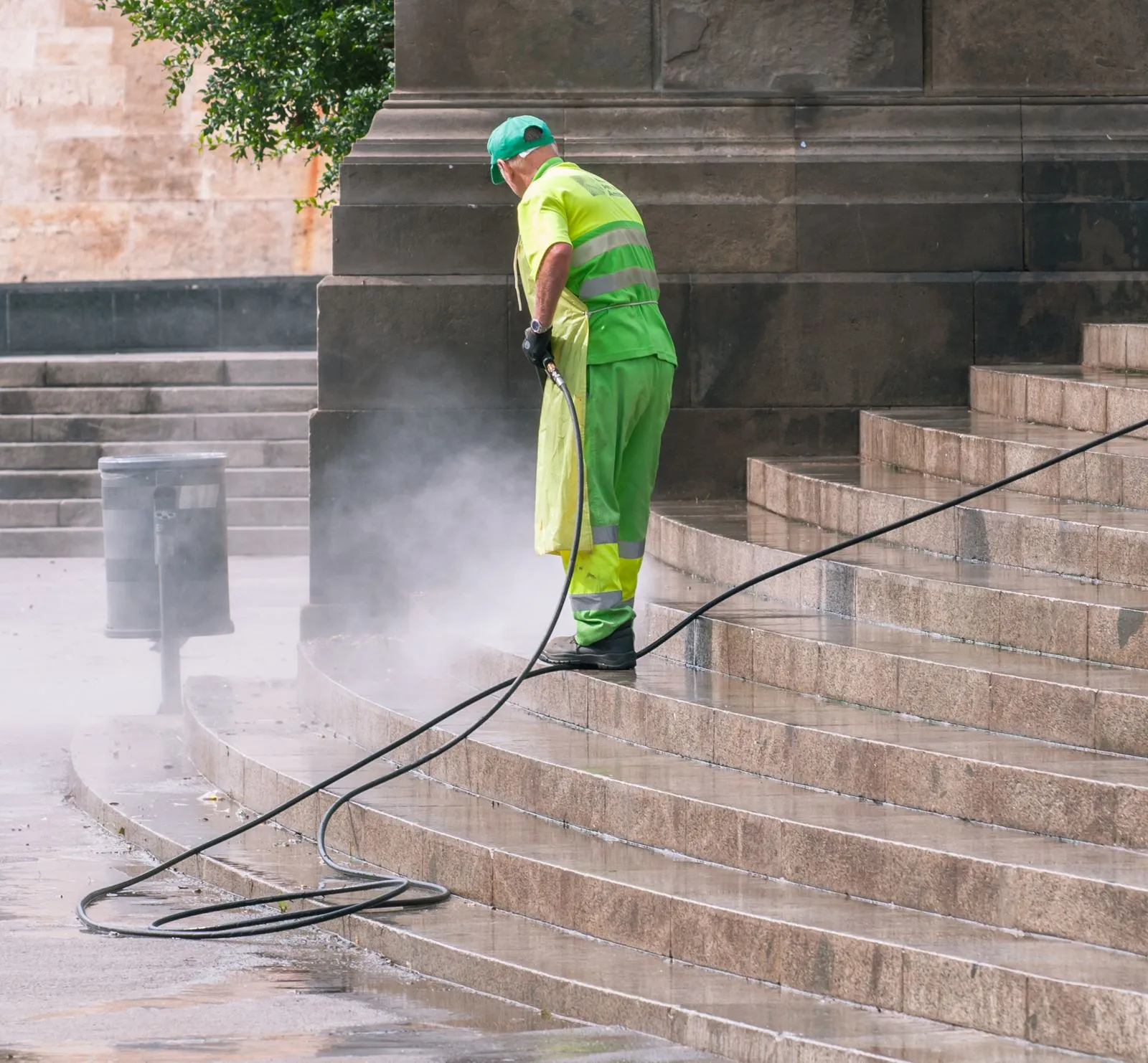 Worker pressure washing stone steps, mist rising off the clean surface